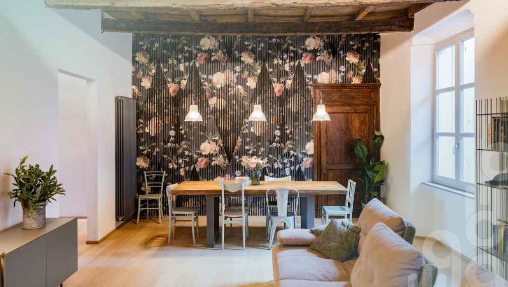 Soggiorno con tavolo in legno, carta da parati floreale e divano chiaro.
