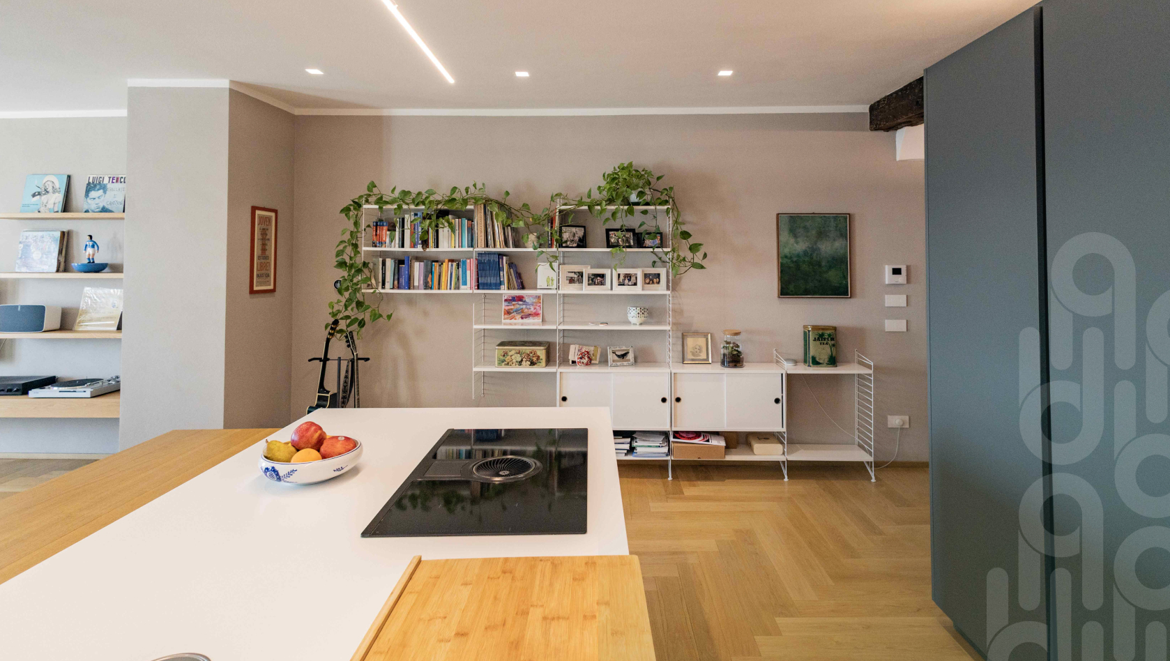Cucina moderna open space con isola bianca, libreria a muro e pavimento in legno.
